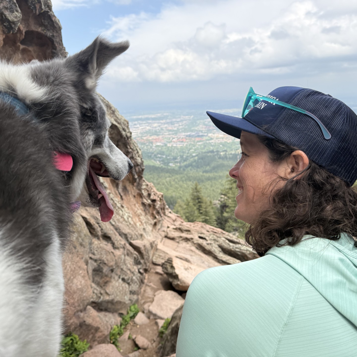 Grace Gamble smiling at her dog while hiking near a rocky overlook with a scenic view in the background